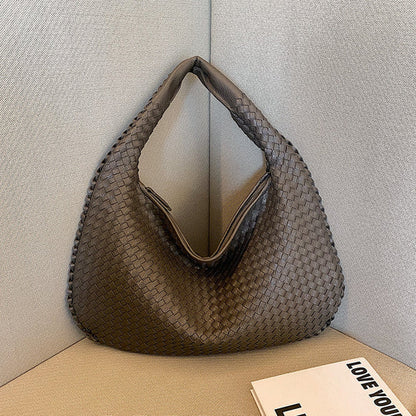 Geflochtene braune Handtasche aus Leder auf Sofa, modisch, elegant, Damenaccessoire.