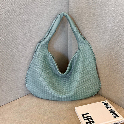 Grüne geflochtene Handtasche aus Leder auf Sofa, modisches Accessoire, stilvoll und elegant.
