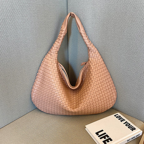 Geflochtene rosa Handtasche aus Leder auf grauem Sofa, modisch, elegant, Damenaccessoire.