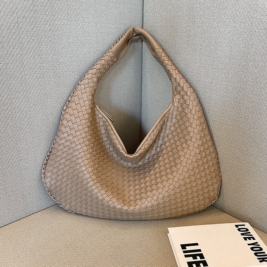 Beigefarbene, geflochtene Handtasche aus Leder auf grauem Sofa, modisch, elegant, Damenaccessoire.