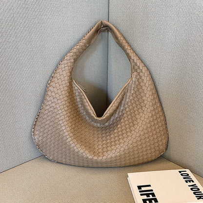Beigefarbene, geflochtene Handtasche aus Leder auf grauem Sofa, modisch, elegant, Damenaccessoire.