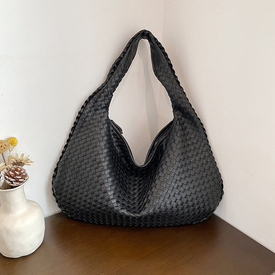 Schwarze geflochtene Handtasche aus Leder auf Holztisch, moderne Damenmode Accessoire.