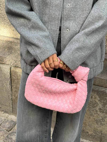 Frau mit grauem Mantel hält rosa geflochtene Handtasche, modisches Accessoire, Streetstyle.