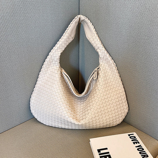 Weiße geflochtene Handtasche aus Leder auf grauem Sofa, stilvoll und modern.
