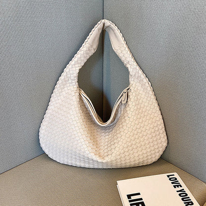 Weiße geflochtene Handtasche aus Leder auf grauem Sofa, stilvoll und modern.