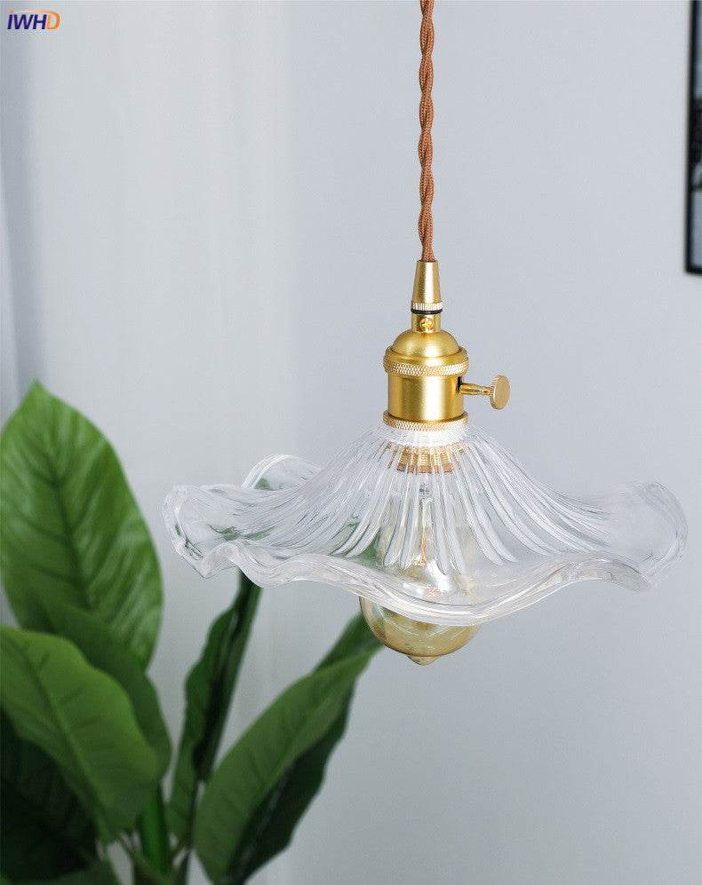 Kronleuchter aus Glas mit Messingfassung, Vintage-Stil, hängend, vor grüner Pflanze.