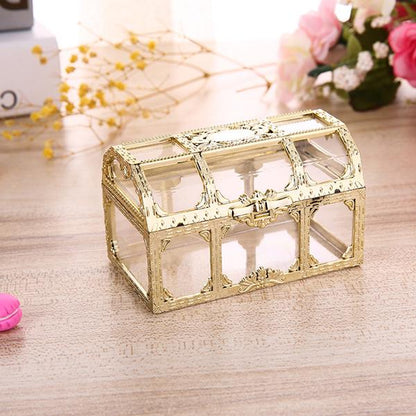 Goldene Schmuckschatulle aus Glas, rechteckig, dekorativ, auf Holztisch mit Blumen im Hintergrund.