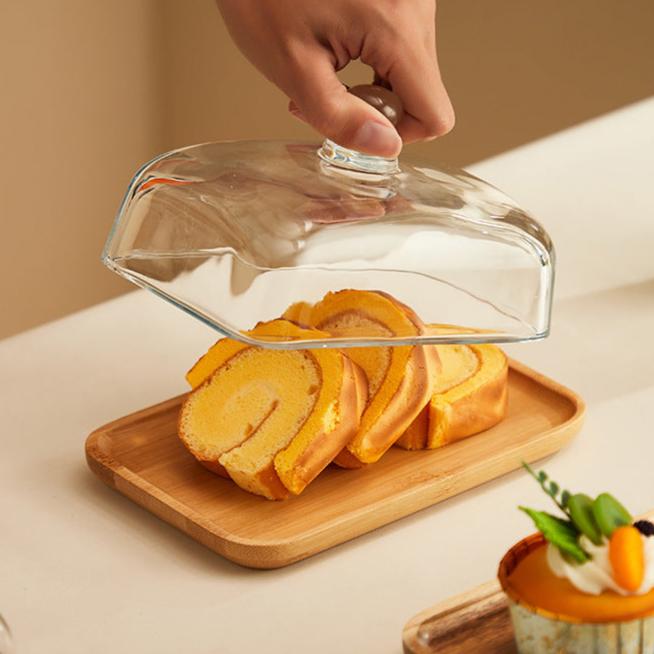 Hand hebt Glasabdeckung von Holztablett mit Kuchenrollen, Dessert, Küche, Serviergeschirr.