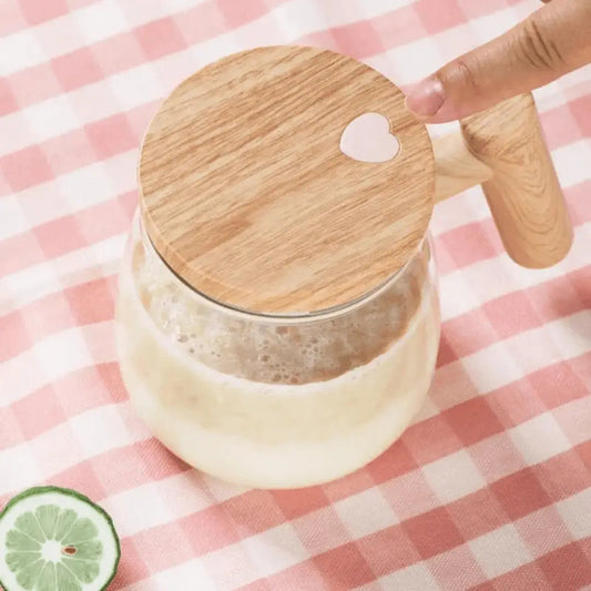 Glaskrug mit Holzdeckel und Herz, gefüllt mit Milchshake, auf rosa-weiß kariertem Tuch.