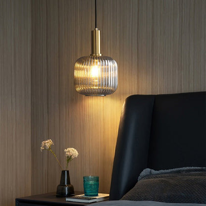 Braune Glas-Hängelampe im dänischen Pastellstil, beleuchtet, neben einem Bett.