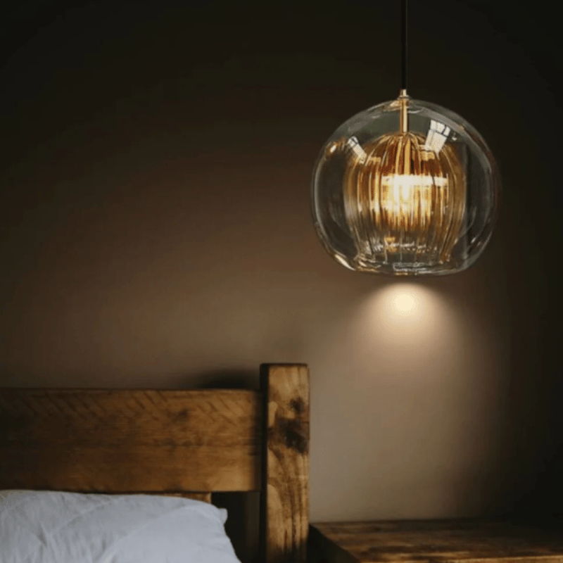 Kugelförmige Glaspendelleuchte über rustikalem Holzbett, warmes Licht, modernes Design.