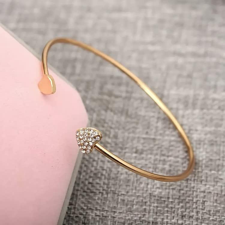Goldenes Armreif mit Herzanhänger, funkelnde Strasssteine, elegantes Schmuckdesign.