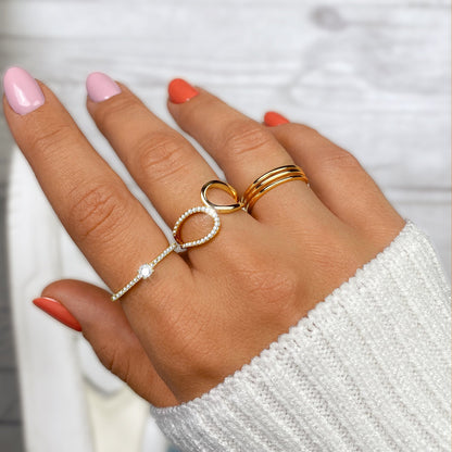 Damenhand mit goldenen und silbernen Ringen, rosa und orange Nägel, weißer Pullover.