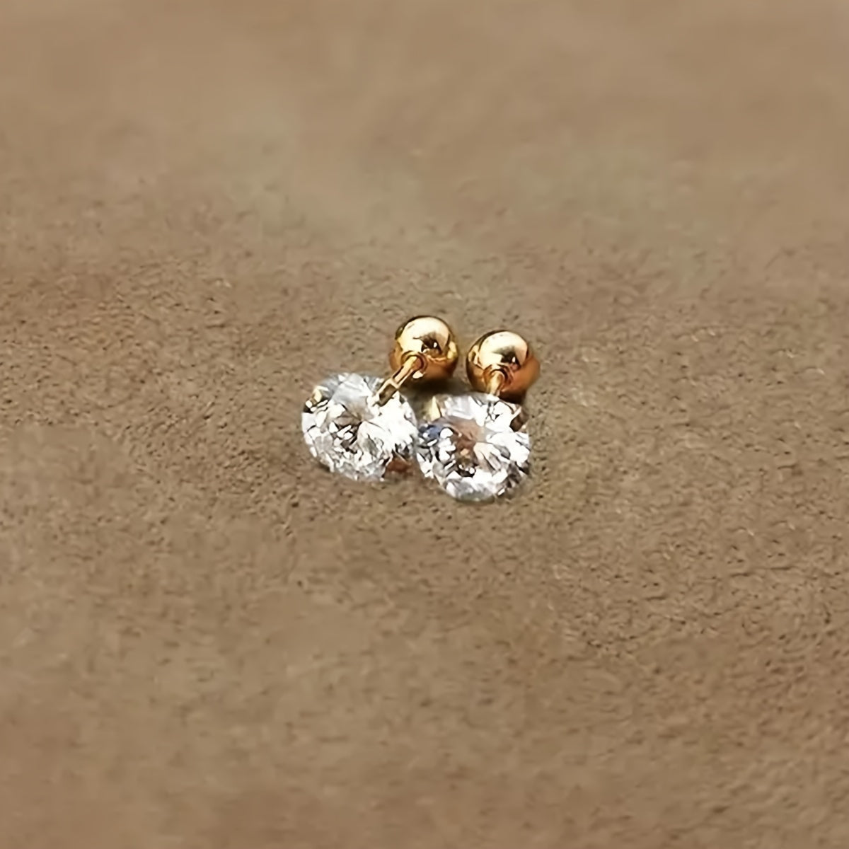 Goldene Ohrringe mit klaren Zirkonia-Steinen auf beigem Hintergrund, eleganter Schmuck.