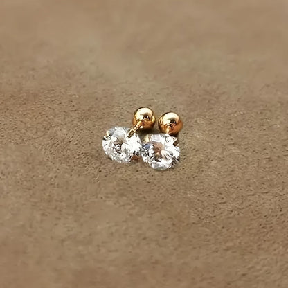 Goldene Ohrringe mit klaren Zirkonia-Steinen auf beigem Hintergrund, eleganter Schmuck.