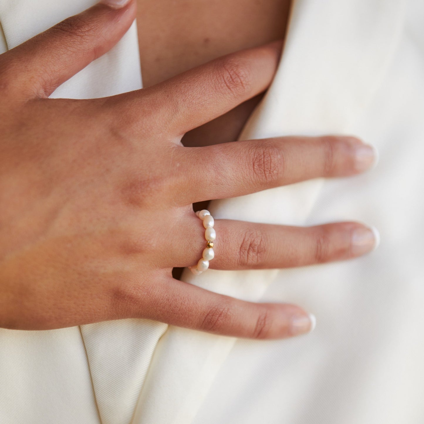Goldener Perlenring auf Finger, eleganter Schmuck, Damenmode, Nahaufnahme.