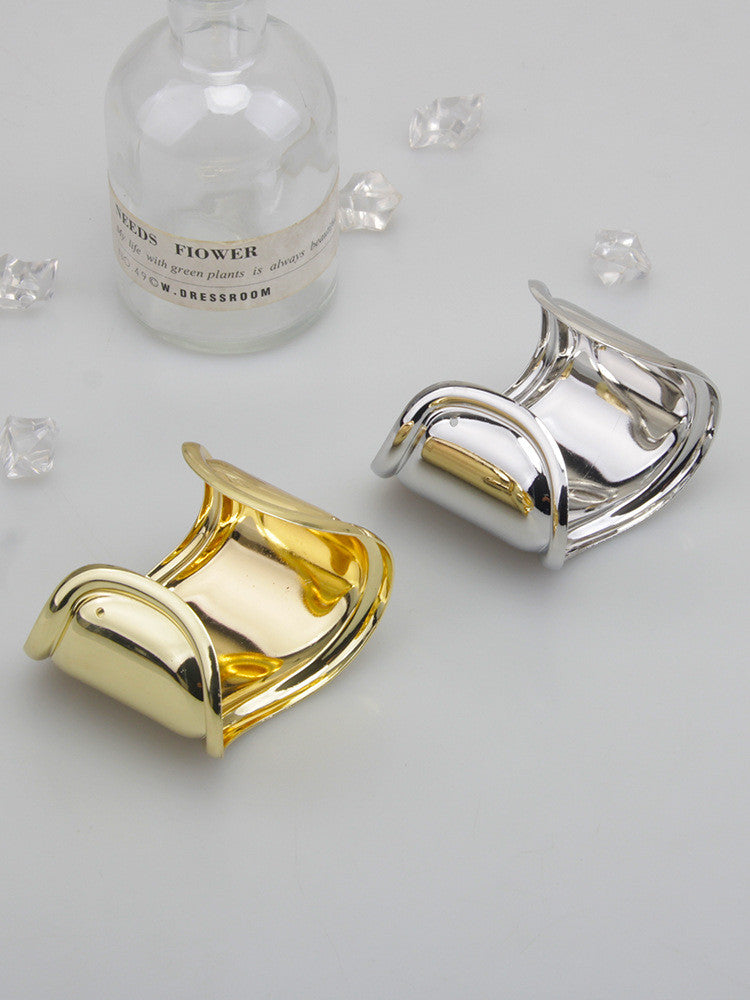 Zwei breite Metallarmbänder, gold und silber, mit asymmetrischem Wellen-Design auf grauem Hintergrund.