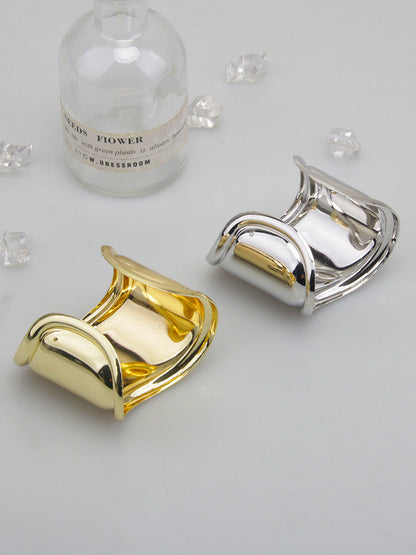 Zwei breite Metallarmbänder, gold und silber, mit asymmetrischem Wellen-Design auf grauem Hintergrund.