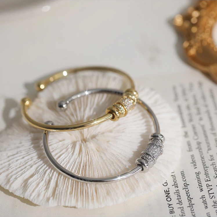 Zwei elegante Armreifen, gold und silber, mit Kristallverzierungen auf hellem Hintergrund.