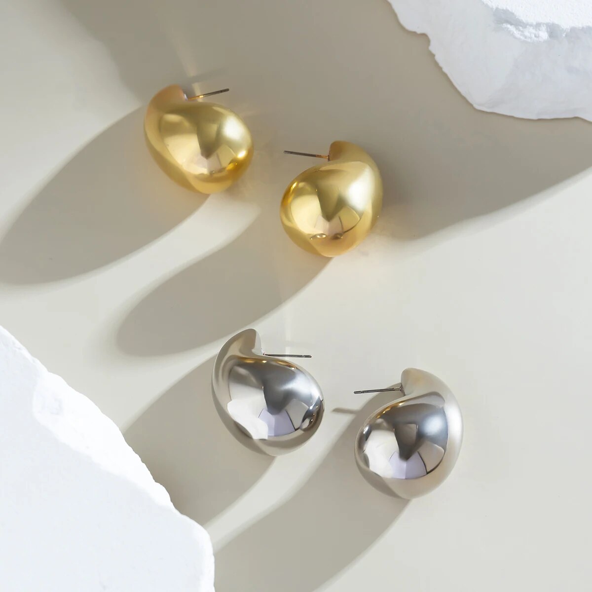 Goldene und silberne Ohrringe, tropfenförmig, glänzend, auf hellem Hintergrund.