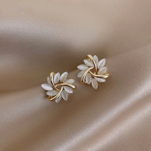 Goldene Ohrringe mit weißen Blättern auf beigem Satin-Hintergrund, eleganter Schmuck.