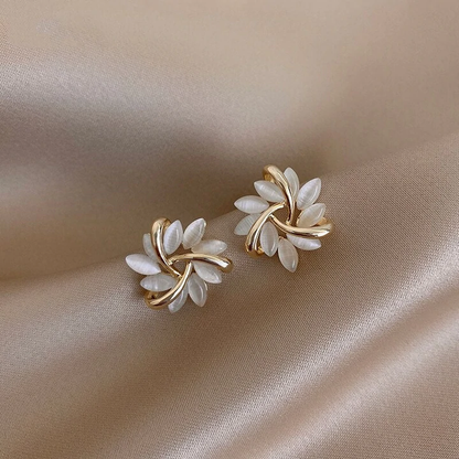 Goldene Ohrringe mit weißen Blättern, elegantes Design, Schmuck auf beigem Stoff.