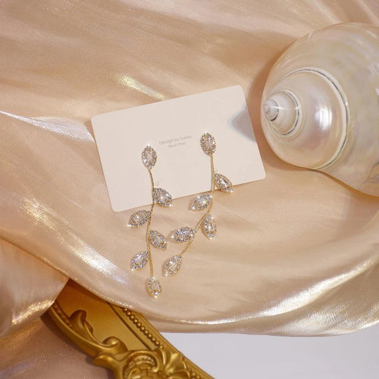 Goldene Ohrringe mit Blattdesign und Kristallen auf schimmerndem Stoff, eleganter Schmuck.
