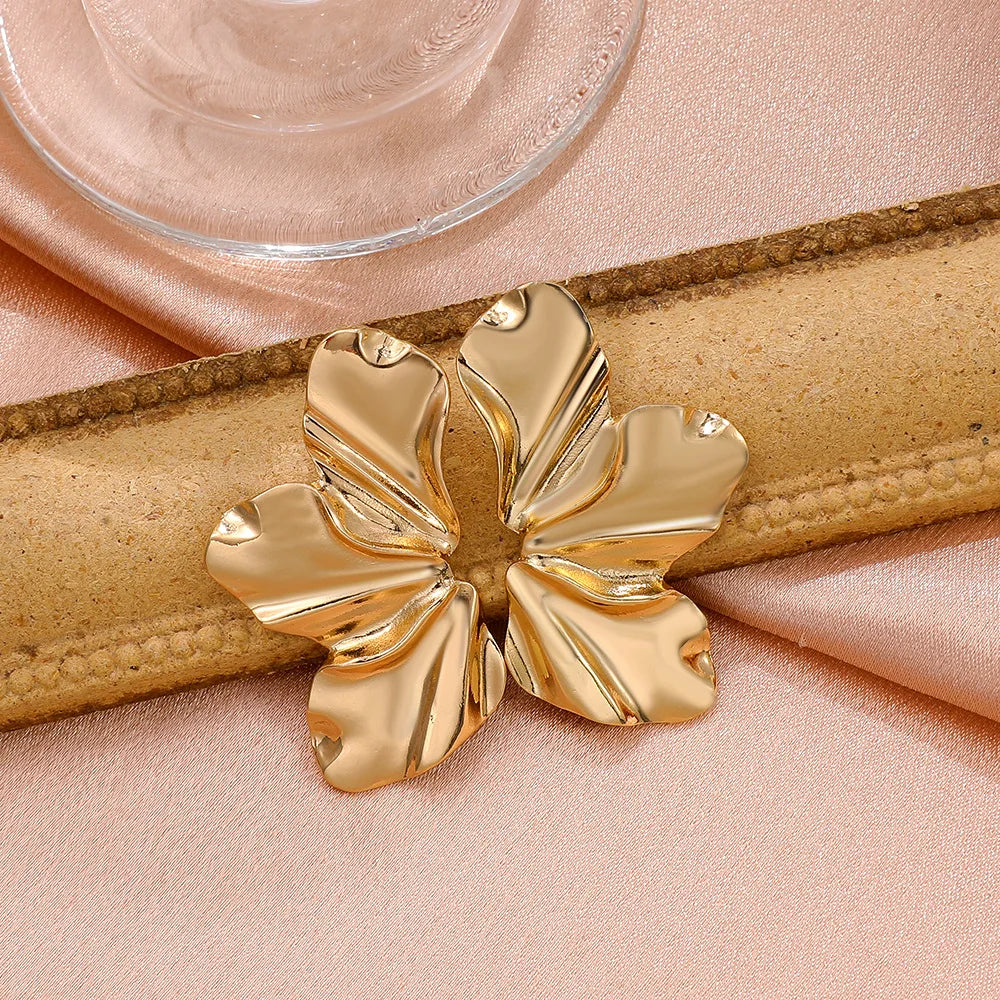 Goldene, blattförmige Ohrringe auf rosa Stoff, eleganter Schmuck, modisches Accessoire.