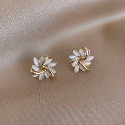 Goldene Ohrringe mit Perlmuttblättern auf beigem Stoff, eleganter Schmuck, Damenaccessoire.