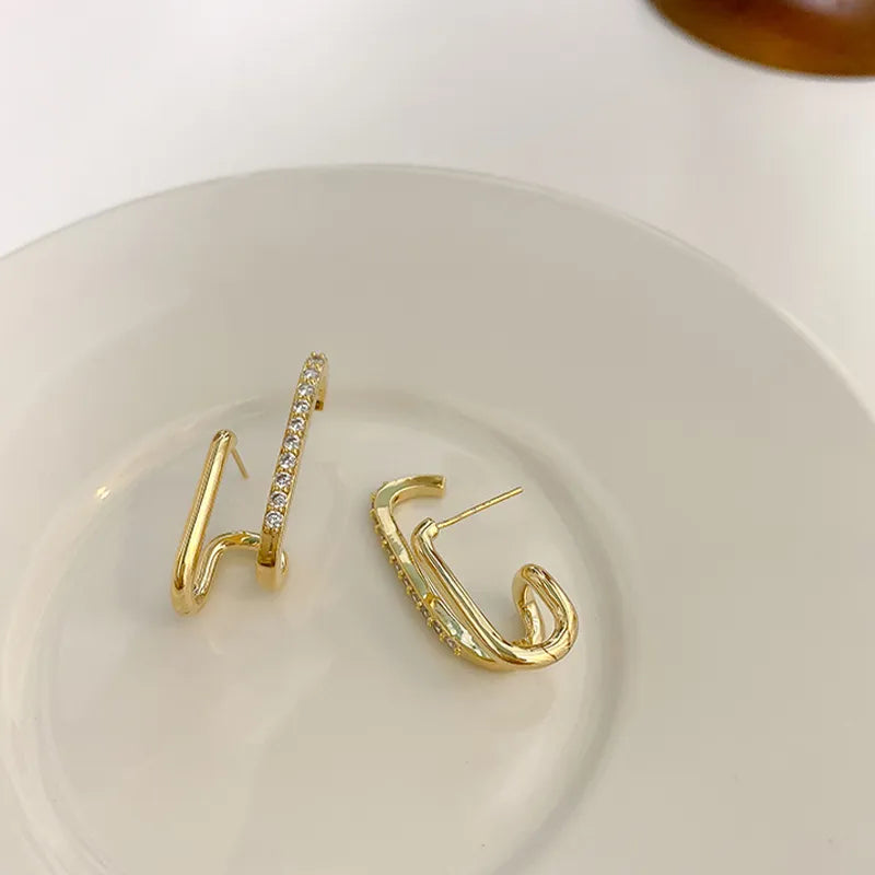 Goldene Ohrringe mit Zirkonia auf weißem Teller, eleganter Schmuck, modisches Accessoire.