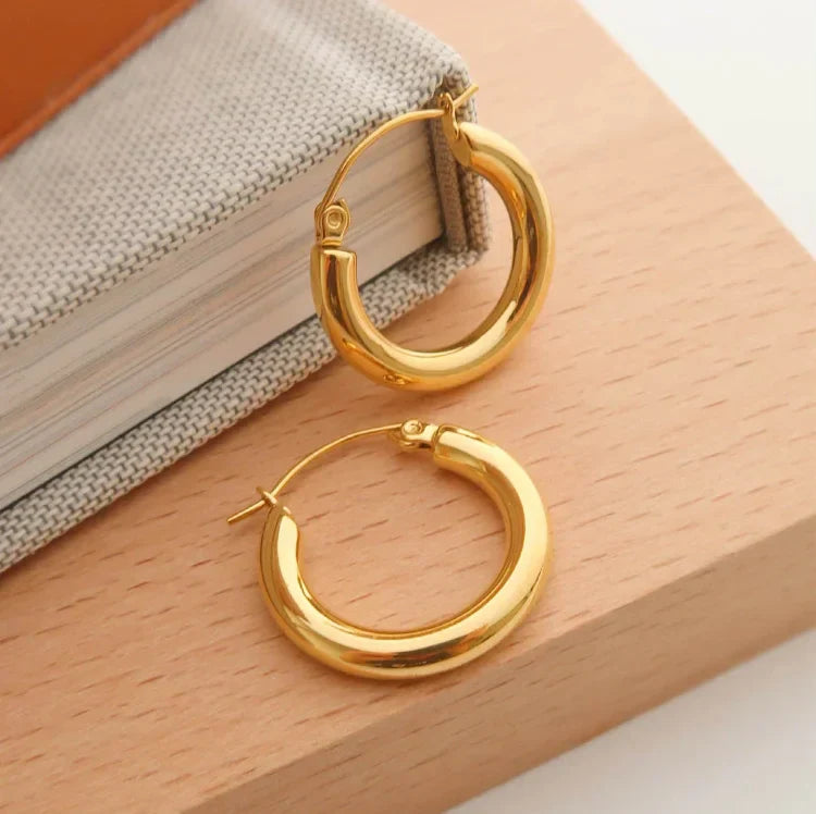 Goldene Creolen Ohrringe auf Holzuntergrund, modisches Schmuckaccessoire für Damen.