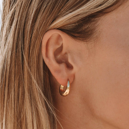 Goldene Creolen-Ohrringe an Ohr, eleganter Schmuck, modisches Accessoire, Damenmode.