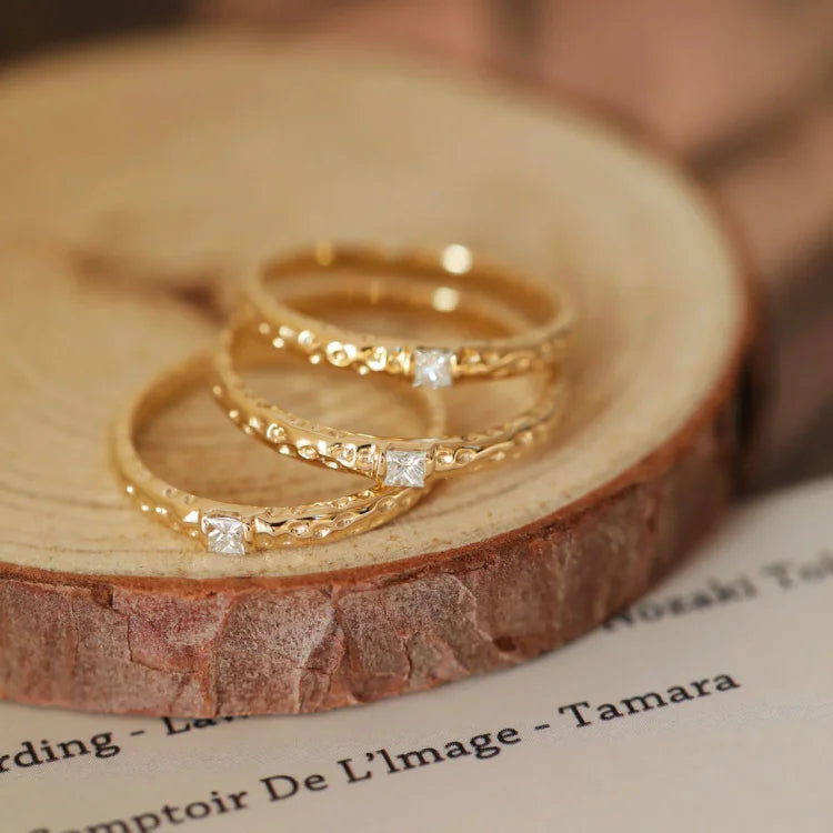Drei goldene Ringe mit Diamanten auf Holzscheibe, eleganter Schmuck, luxuriöses Design.