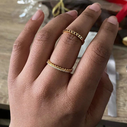Goldene Ringe an Hand, einer mit Kettendesign, der andere mit Strasssteinen, auf Holztisch.