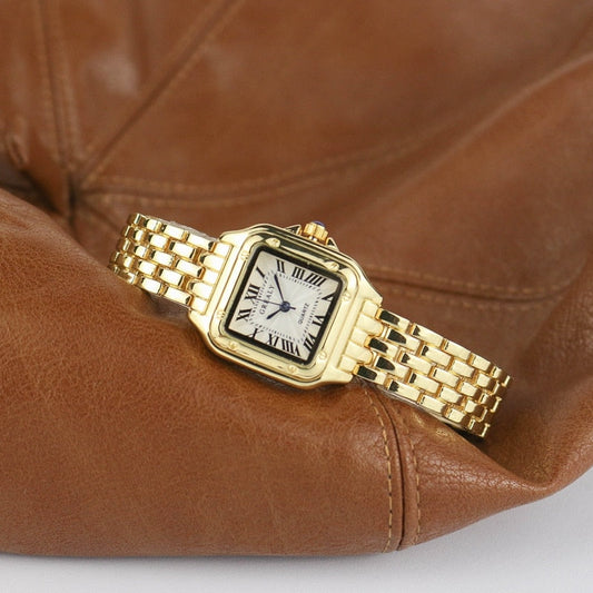 Goldene Armbanduhr mit römischen Ziffern auf braunem Lederhintergrund.