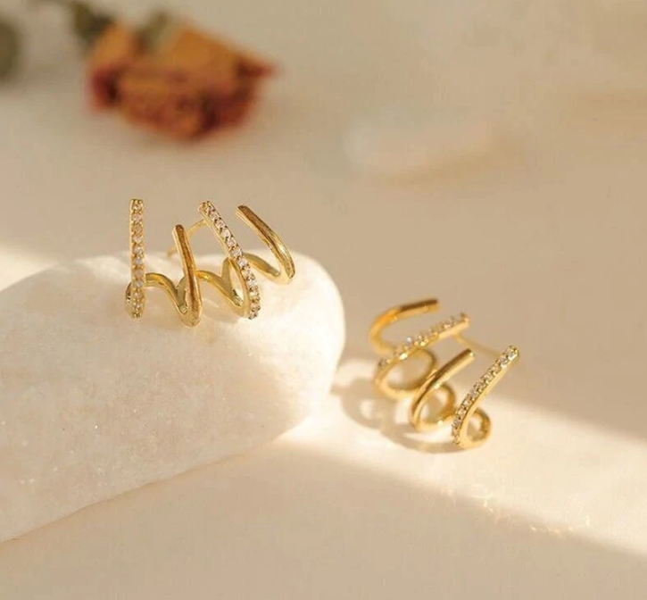 Goldene Spiralringe mit Strasssteinen auf weißem Hintergrund, eleganter Schmuck für Damen.