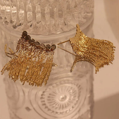 Goldene Quasten-Ohrringe auf Glasoberfläche, eleganter Schmuck, modisches Accessoire.
