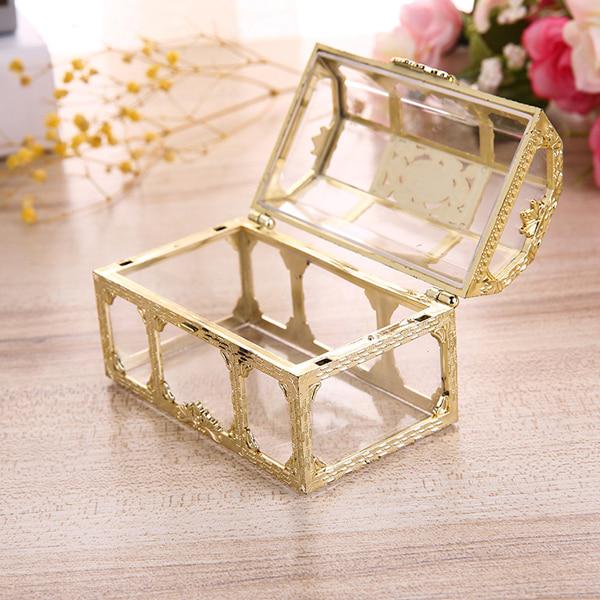Goldene Schmuckschatulle aus Glas, rechteckig, offen, auf Holztisch mit Blumen im Hintergrund.
