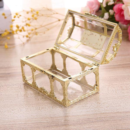 Goldene Schmuckschatulle aus Glas, rechteckig, offen, auf Holztisch mit Blumen im Hintergrund.