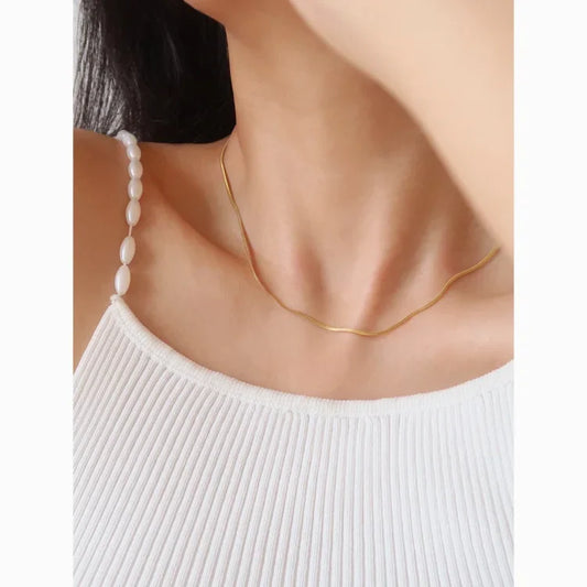 Frau trägt goldene Halskette und weißes geripptes Top, eleganter Schmuck, minimalistisch.