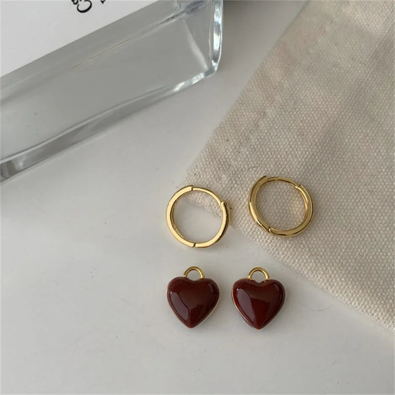 Goldene Creolen mit roten Herzanhängern auf beigem Stoff, eleganter Schmuck für Damen.