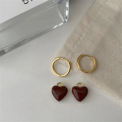 Goldene Creolen mit roten Herzanhängern auf beigem Stoff, eleganter Schmuck für Damen.