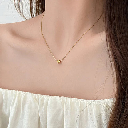 Frau mit goldener Herz-Halskette, elegantes Schmuckstück, minimalistisch, modisch, Geschenkidee.
