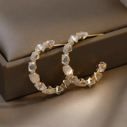 Goldene Creolen mit weißen und klaren Kristallen, eleganter Schmuck, modische Ohrringe.