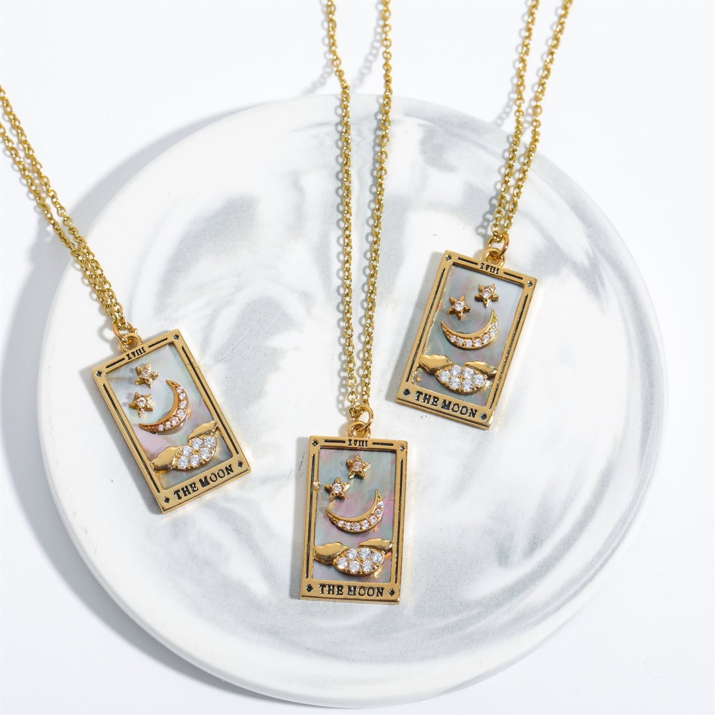 Drei goldene Tarot-Halsketten mit Mondmotiv auf weißem Teller.
