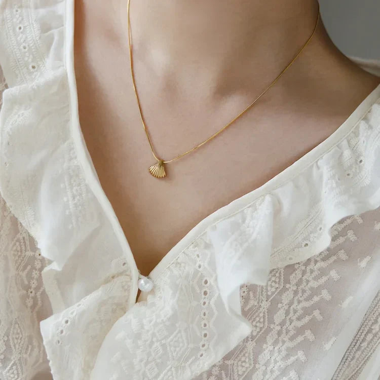 Goldene Muschel-Halskette auf weißer Spitzenbluse, eleganter Schmuck für Damen.