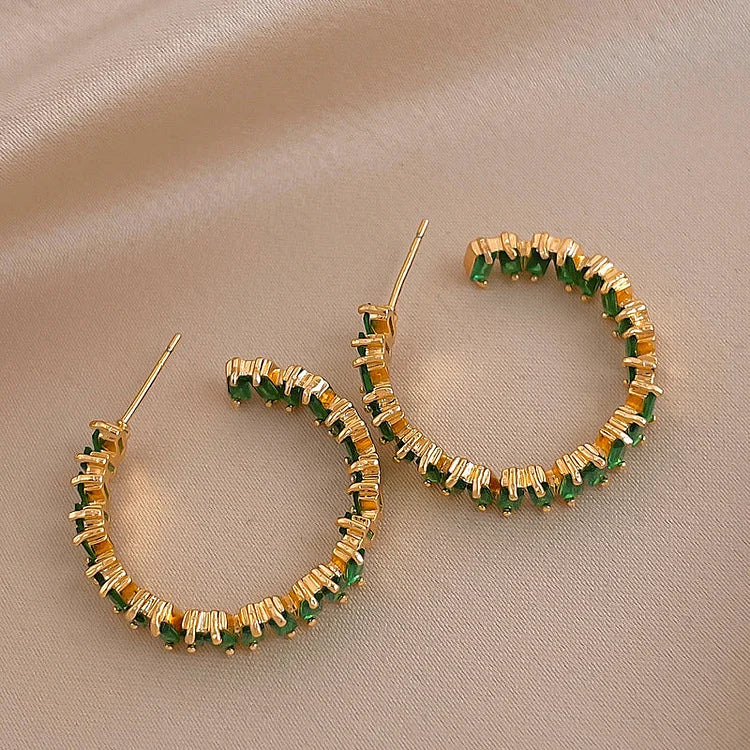 Goldene Creolen mit grünen Steinen, eleganter Schmuck, modische Ohrringe, luxuriöses Design.