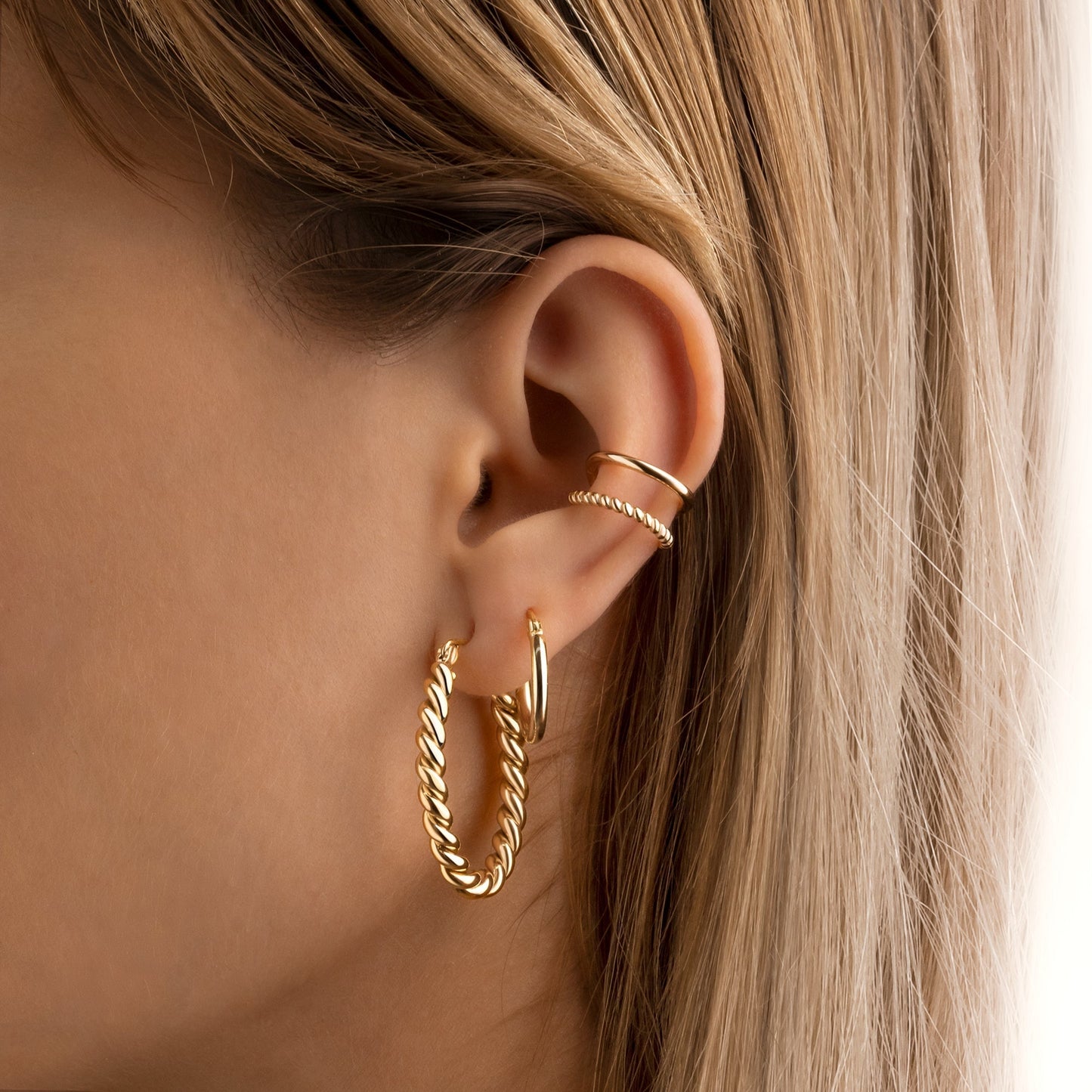 Frau mit goldenen Creolen und Ohrsteckern, modischer Schmuck, Nahaufnahme, elegantes Design.