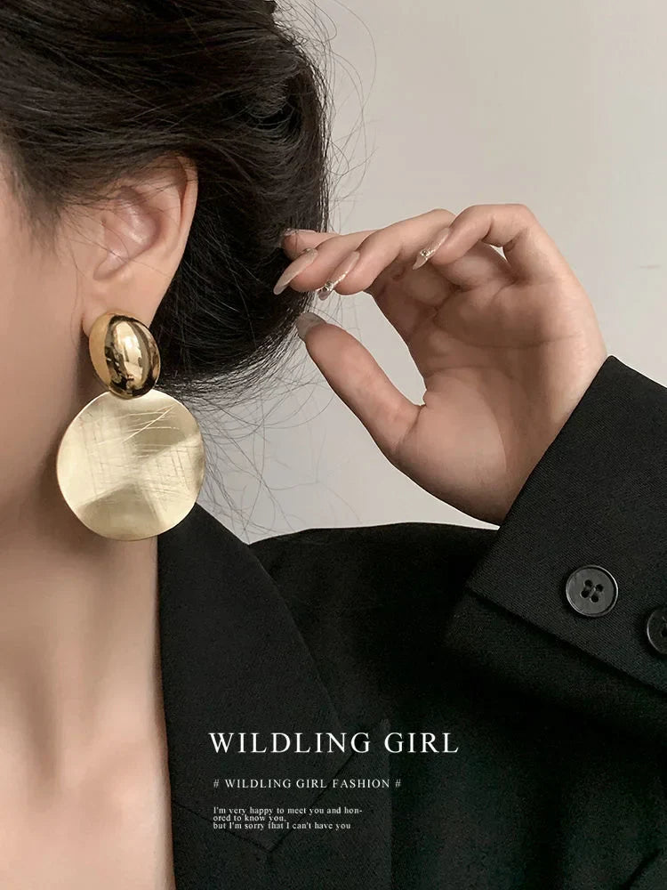 Frau mit großen, goldenen Ohrringen und schwarzem Blazer, elegante Modeaccessoires.