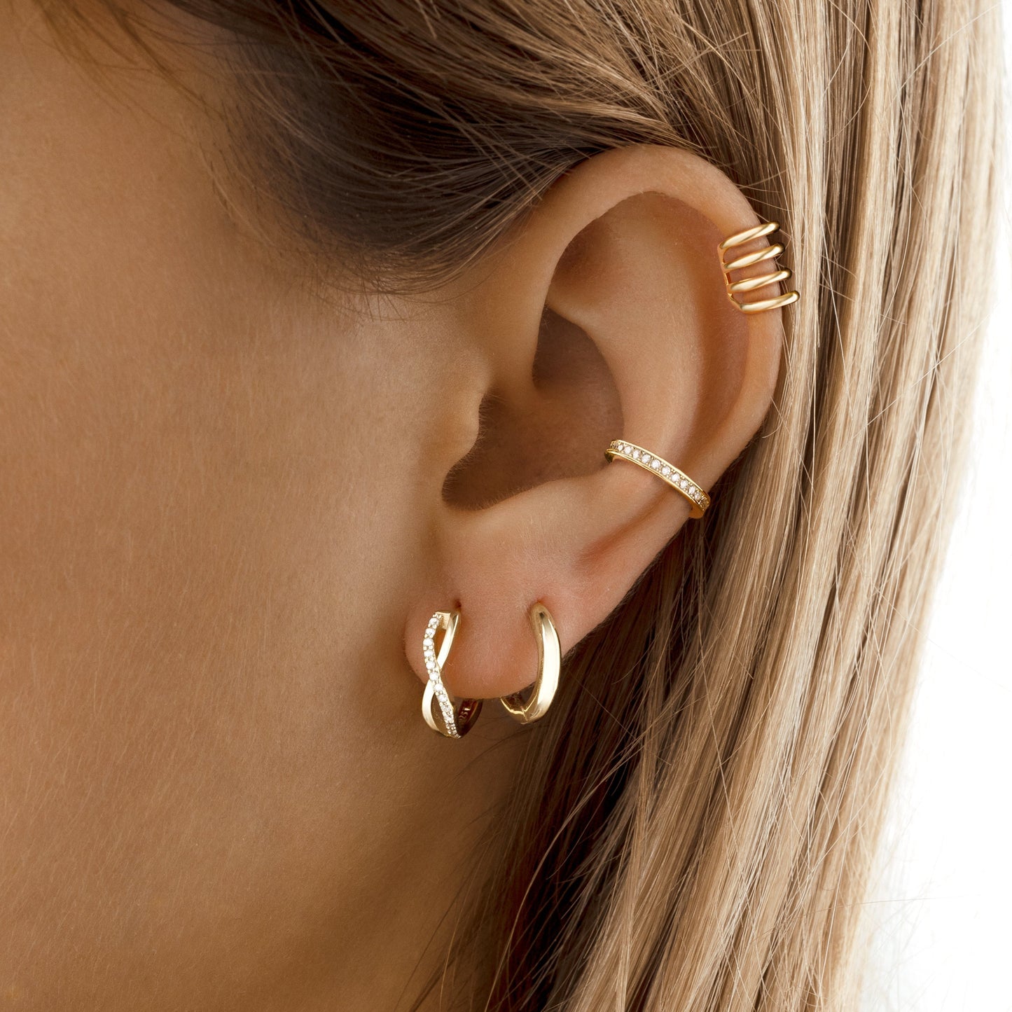 Frauenohr mit goldenen Creolen und Ohrmanschette, modischer Schmuck, Nahaufnahme.